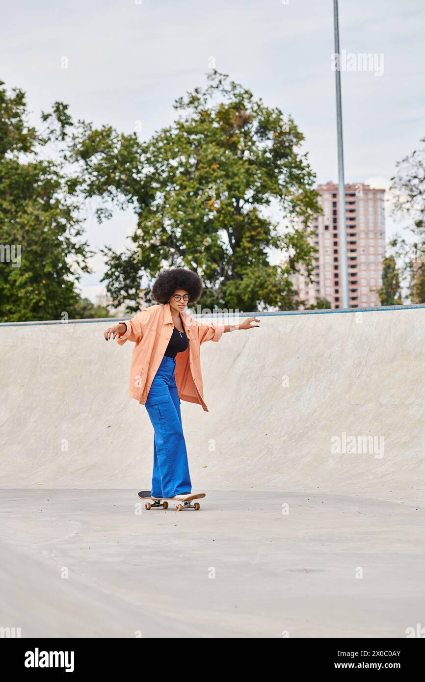 A young African American woman with curly hair confidently rides a skateboard down a challenging cement ramp in a skate park. Stock Photo
