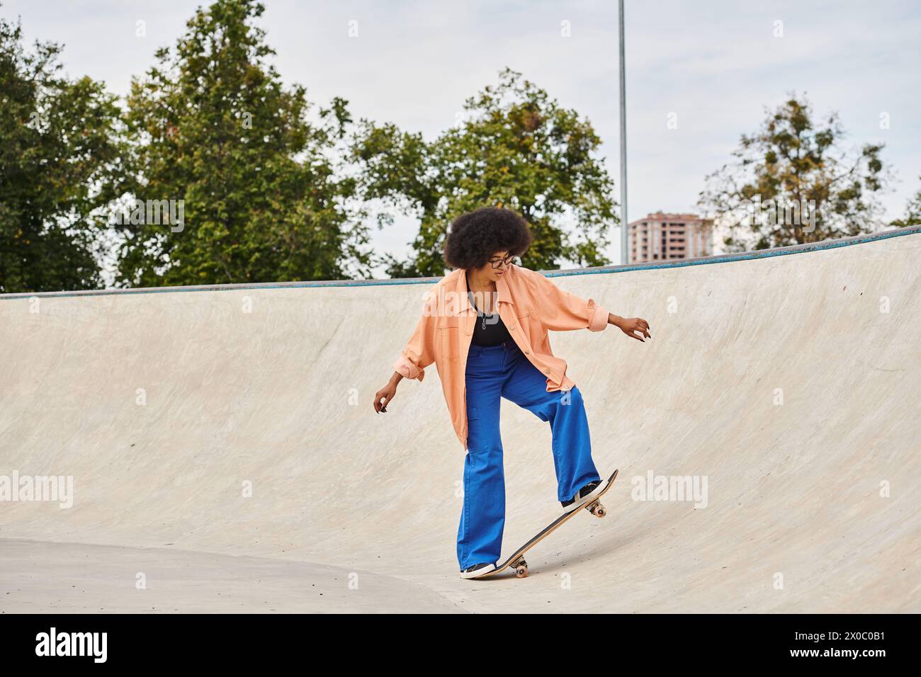 A young African American woman with curly hair boldly rides her skateboard up the side of a ramp at the skate park. Stock Photo