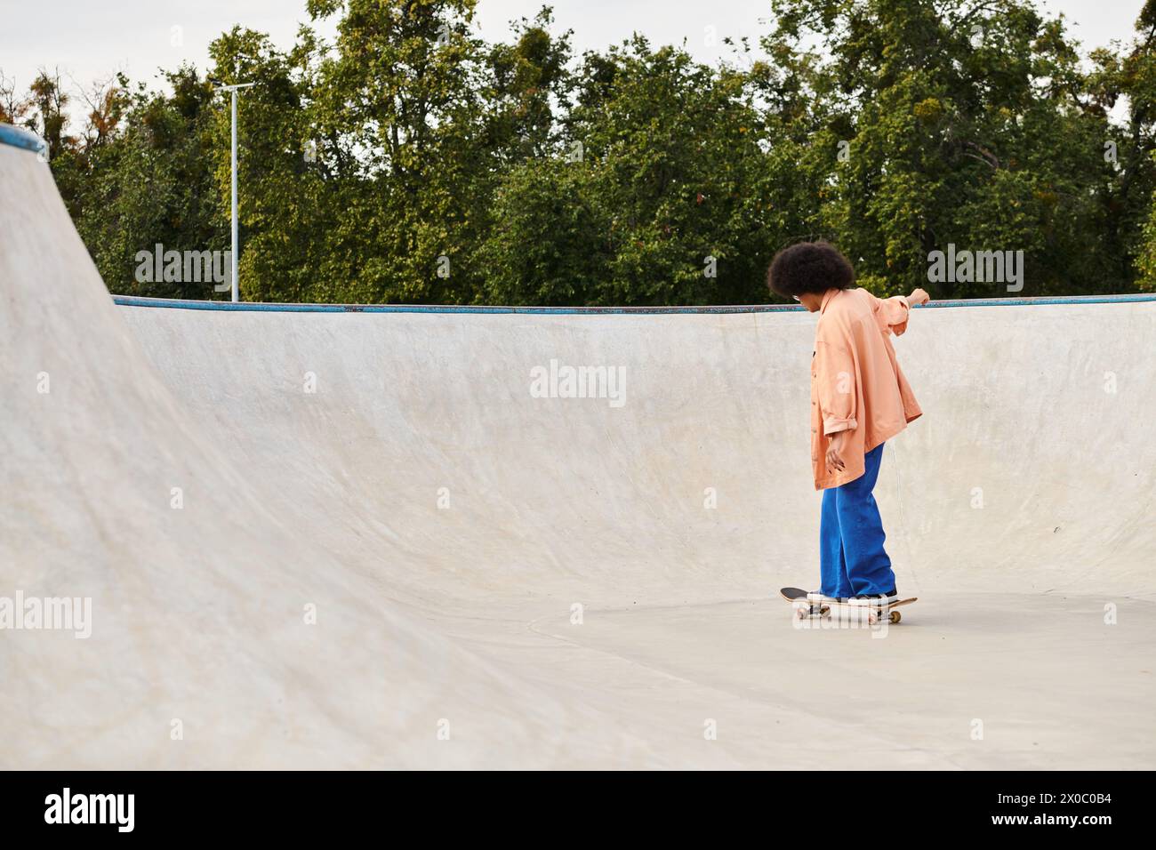 A young African American woman with curly hair skateboarding at a skate park, performing tricks on the ramps and rails. Stock Photo