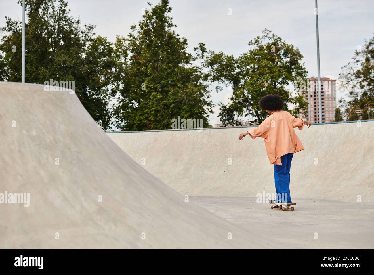 Young African American woman with curly hair rides skateboard in a bright and lively outdoor skate park setting. Stock Photo
