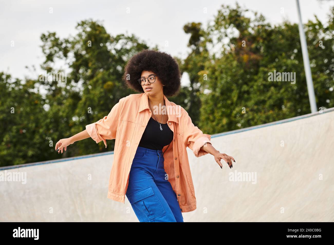 A determined young African American woman with curly hair riding a skateboard up the side of a ramp at an outdoor skate park. Stock Photo