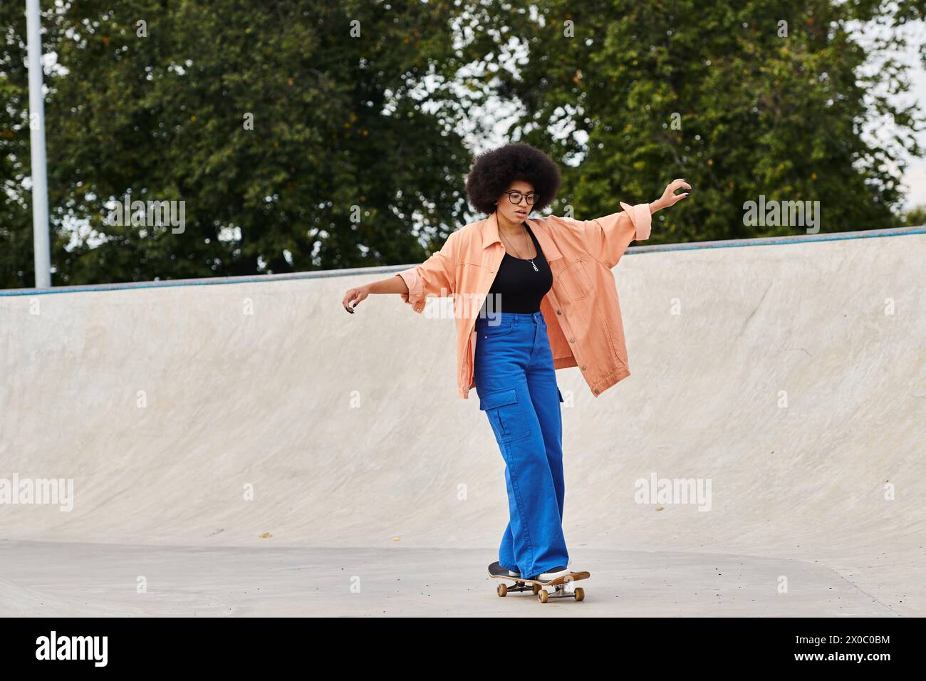 A young African American woman with curly hair confidently rides a skateboard at a vibrant skate park. Stock Photo