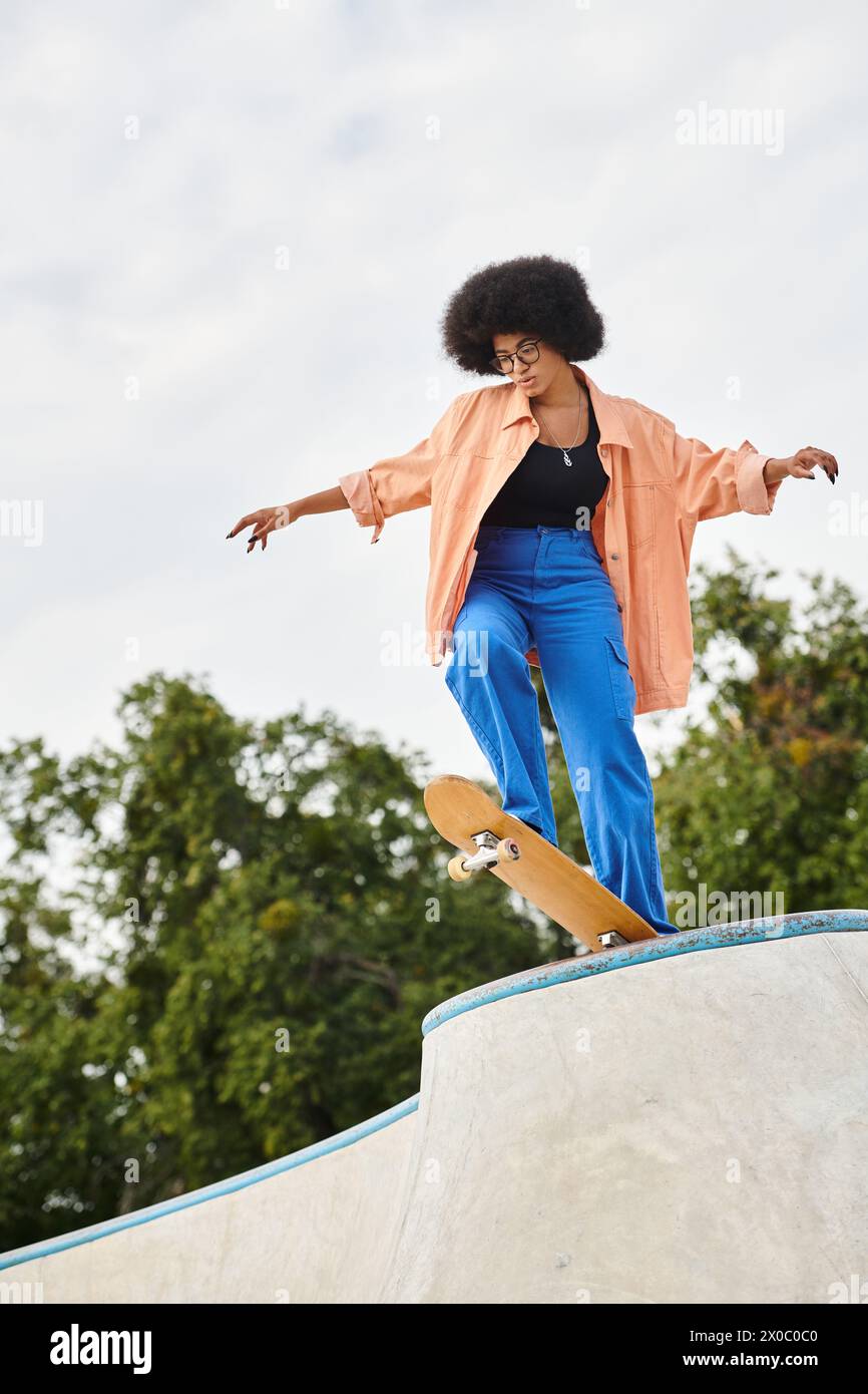 An African American woman with curly hair confidently rides a skateboard up the side of a ramp at an outdoor skate park. Stock Photo