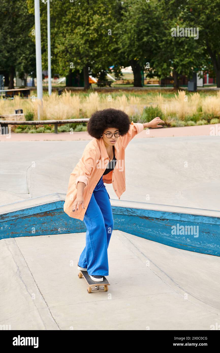 Young African American woman with curly hair rides skateboard down cement ramp at outdoor skate park. Stock Photo
