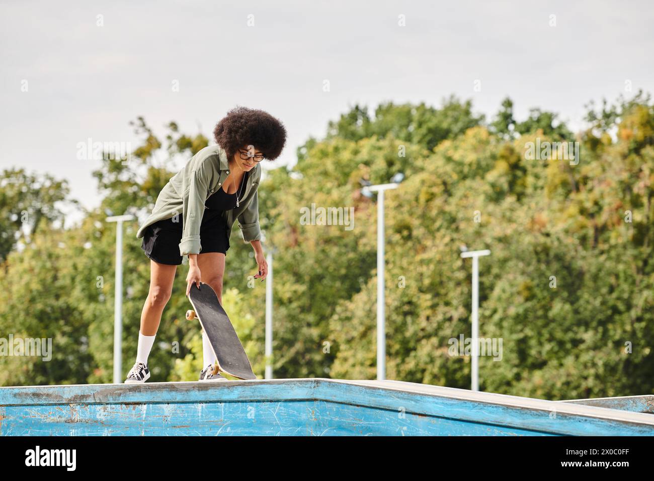 A talented young African American woman with curly hair skateboards by the edge of a pool in a dynamic and daring move. Stock Photo