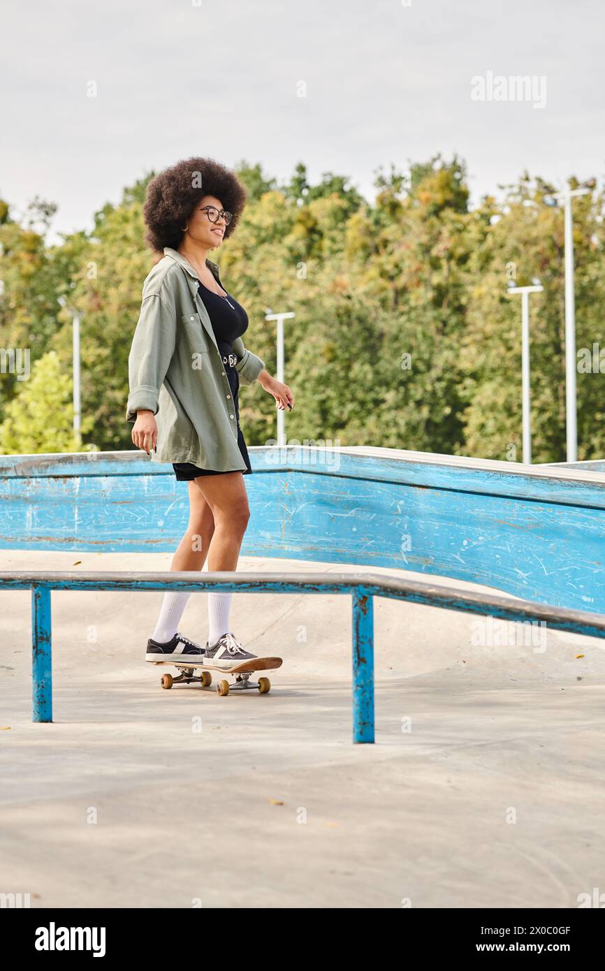 Young African American woman with curly hair rides a skateboard fearlessly on a metal rail at an outdoor skate park. Stock Photo