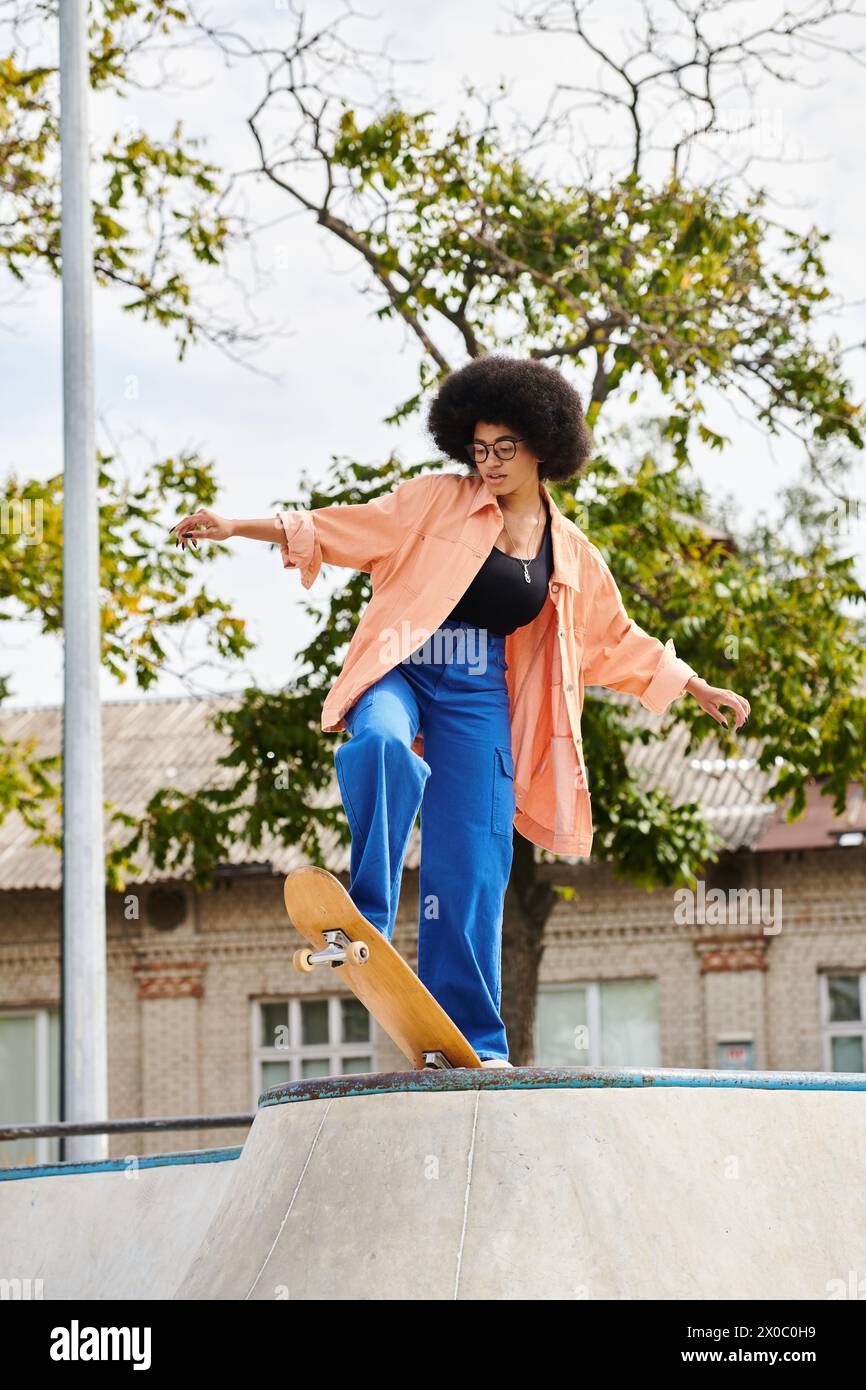 A young African American woman with curly hair skillfully rides a skateboard up the side of a ramp at an outdoor skate park. Stock Photo