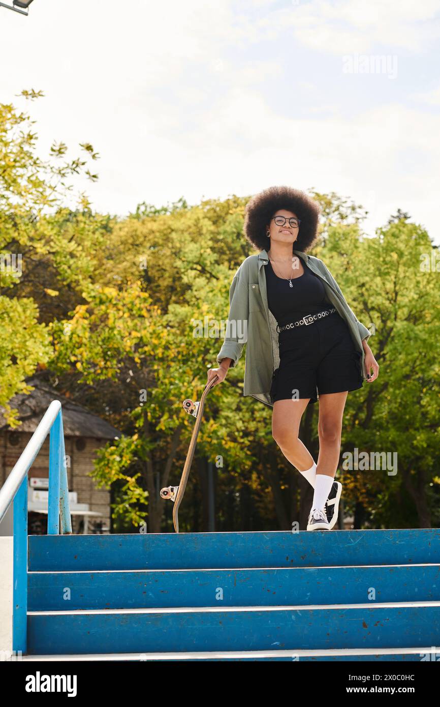 A young African American woman with curly hair confidently climbs a flight of stairs while holding a skateboard. Stock Photo