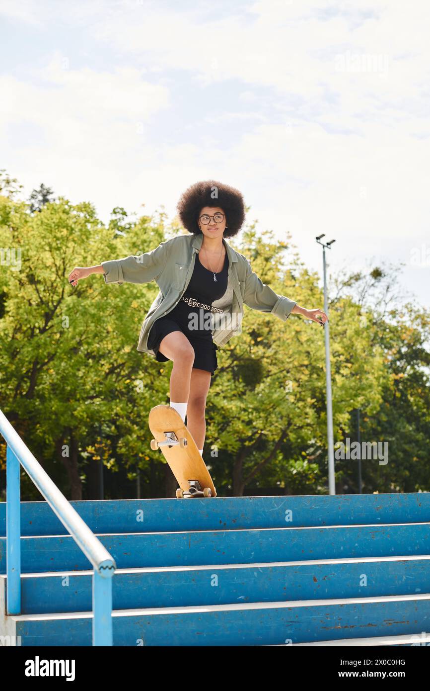 A young African American woman with curly hair skateboards down an urban flight of stairs in a skate park. Stock Photo