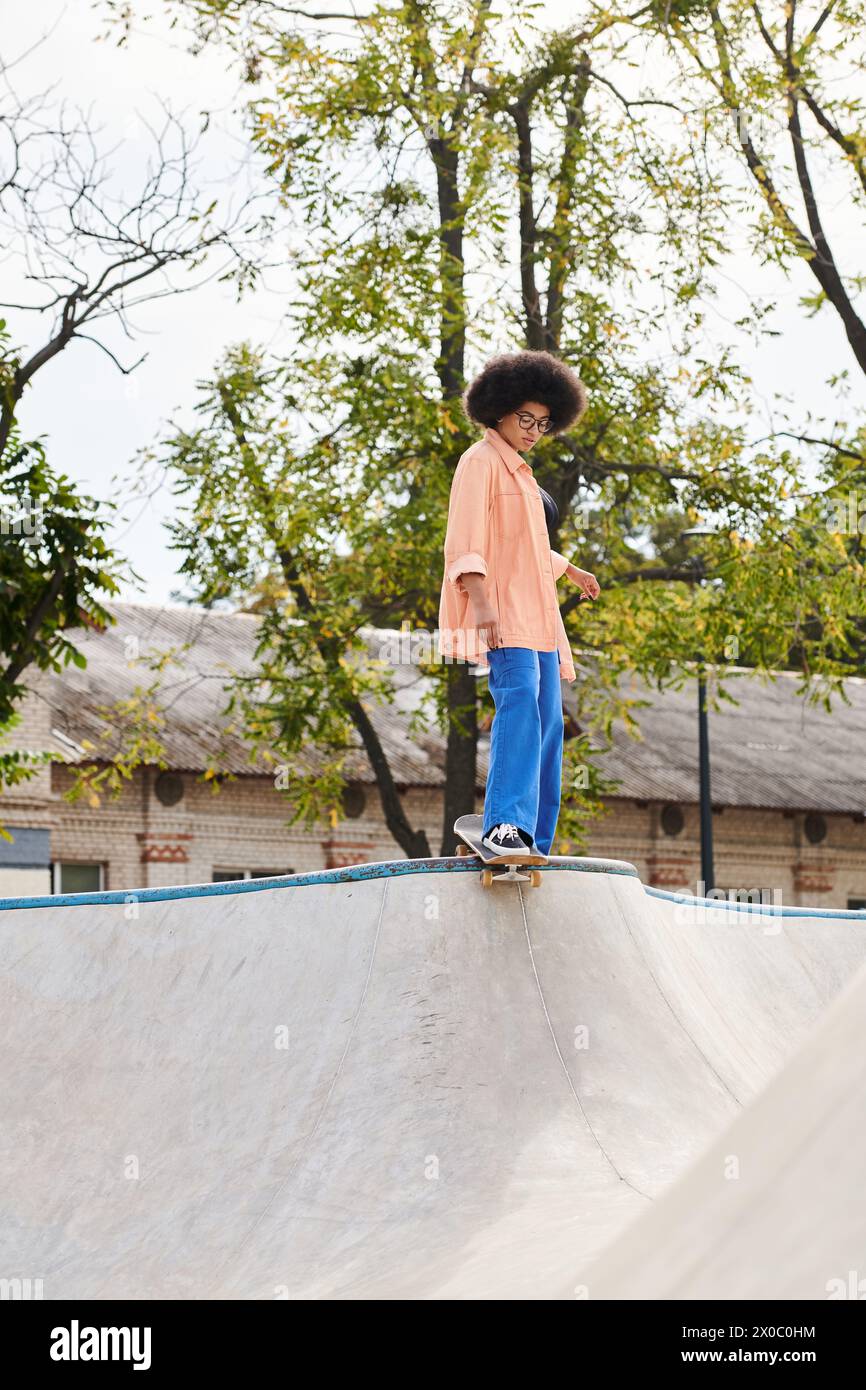 A young man with curly hair is skillfully riding a skateboard on top of a ramp in a skate park, showcasing his impressive tricks and maneuvers. Stock Photo