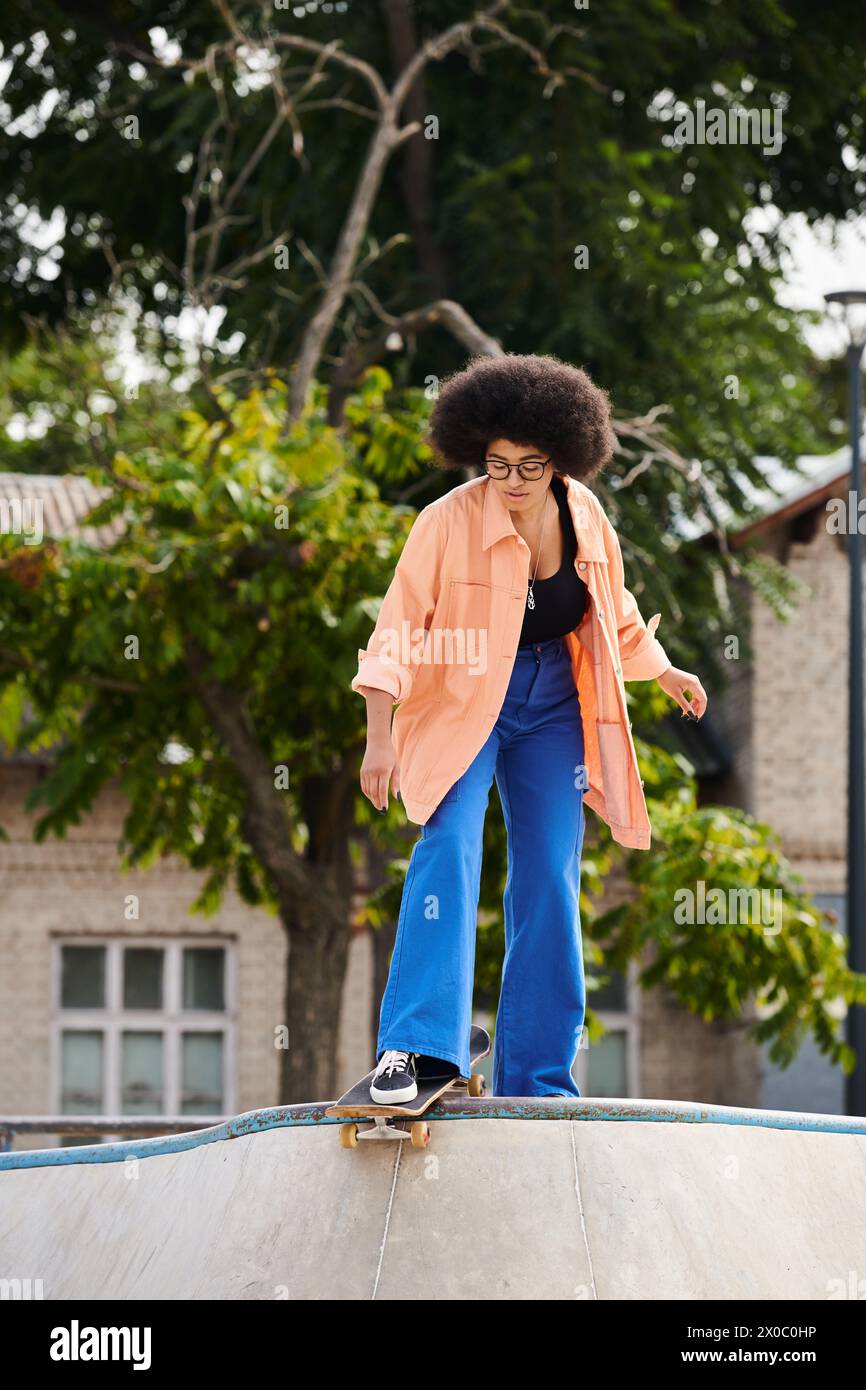 A young African American woman with curly hair skillfully rides a skateboard on a ramp at an outdoor skate park. Stock Photo