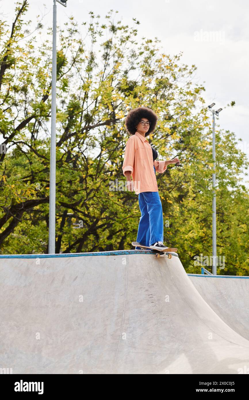 A young African American woman with curly hair riding a skateboard on a ramp at a skate park, displaying skill and style. Stock Photo