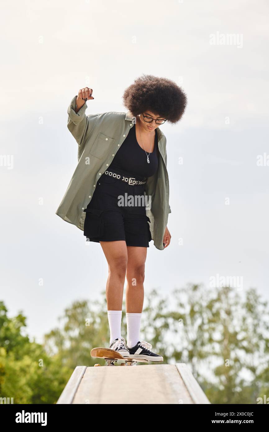 An African American woman with curly hair rides a skateboard on a wooden ramp at a skate park. Stock Photo