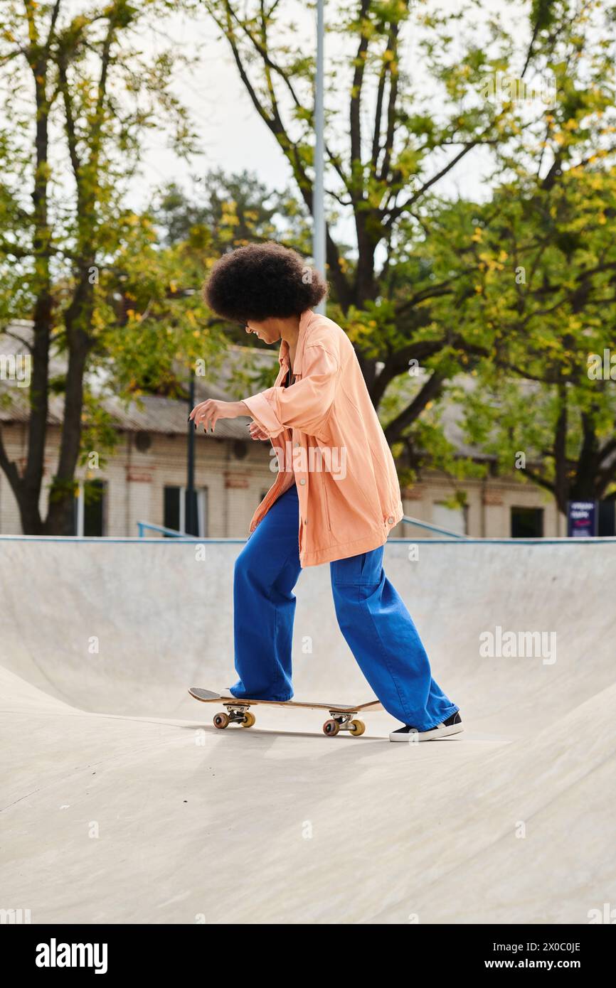 A young African American woman with curly hair glides down a ramp on a skateboard in an outdoor skate park. Stock Photo