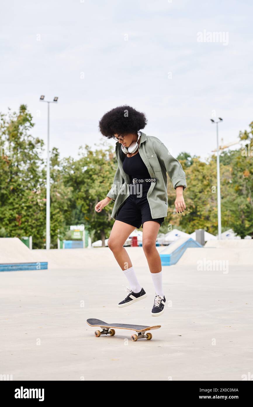 Young African American woman with curly hair skateboarding in a skate park on a cement surface. Stock Photo