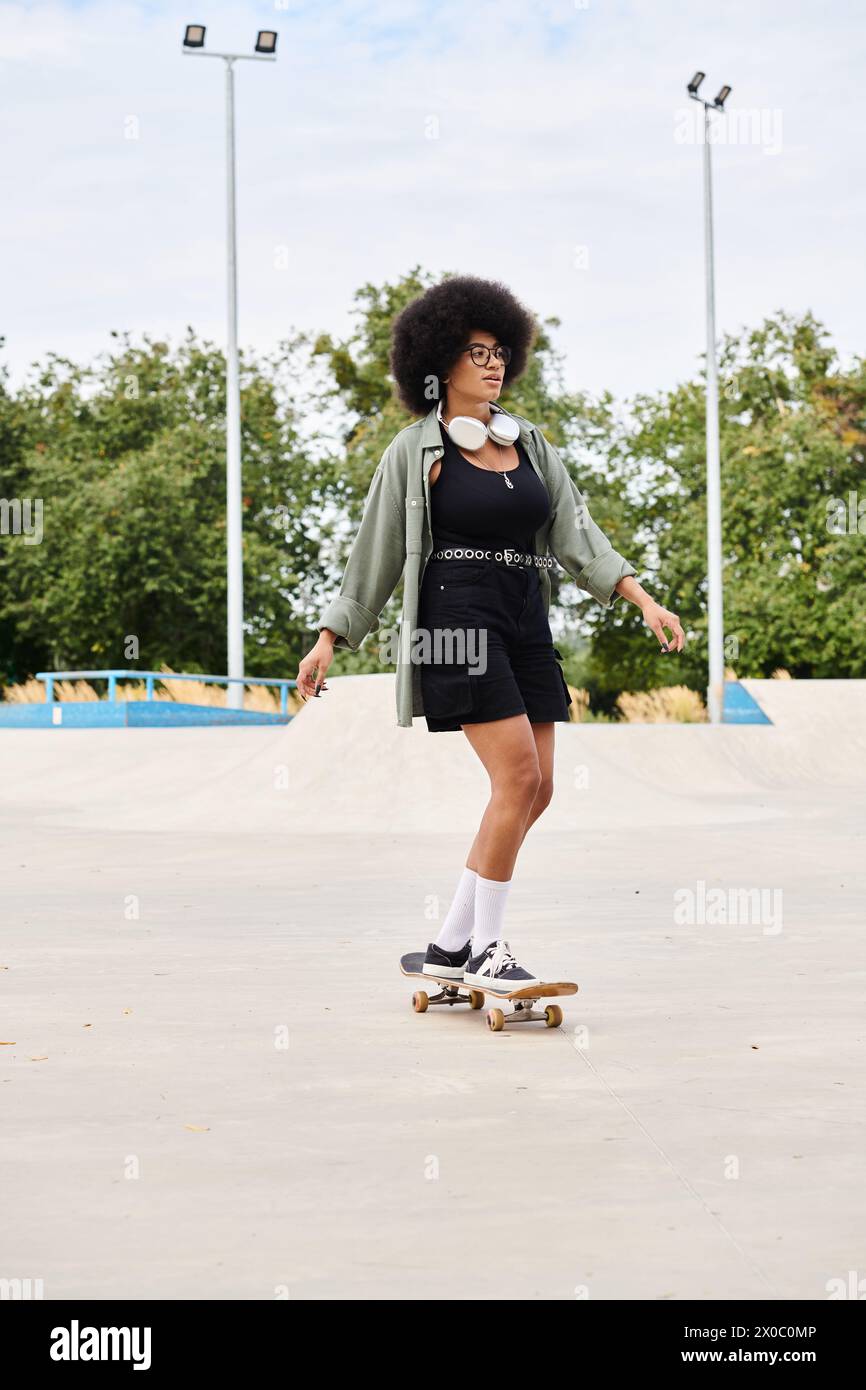 A skilled young African American woman with curly hair skateboards gracefully on top of a cement field in a skate park. Stock Photo