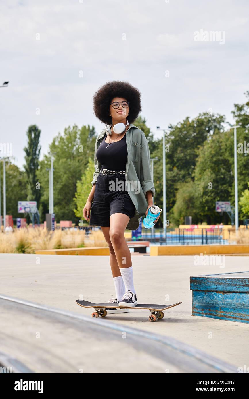 A young African American woman with curly hair gracefully skateboards down a ramp at an outdoor skate park. Stock Photo