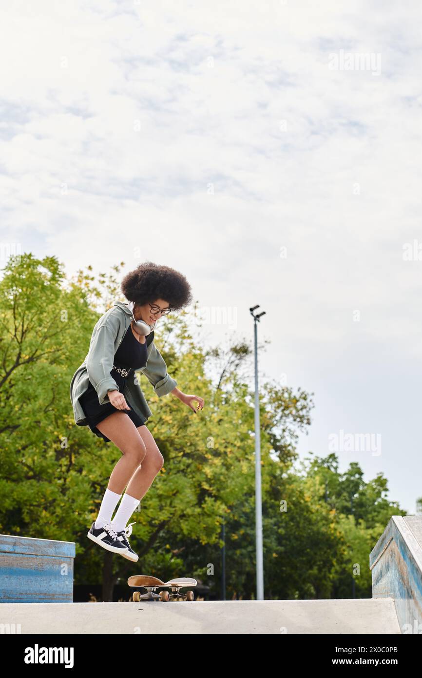A young African American woman with curly hair skillfully skateboarding up the side of a ramp at an outdoor skate park. Stock Photo