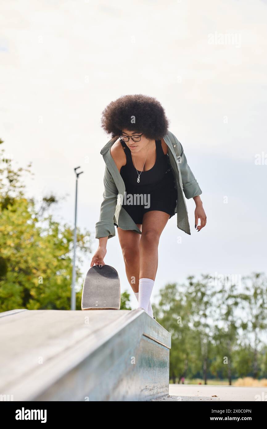 A young African American woman with curly hair glides on a skateboard in a skate park. Stock Photo