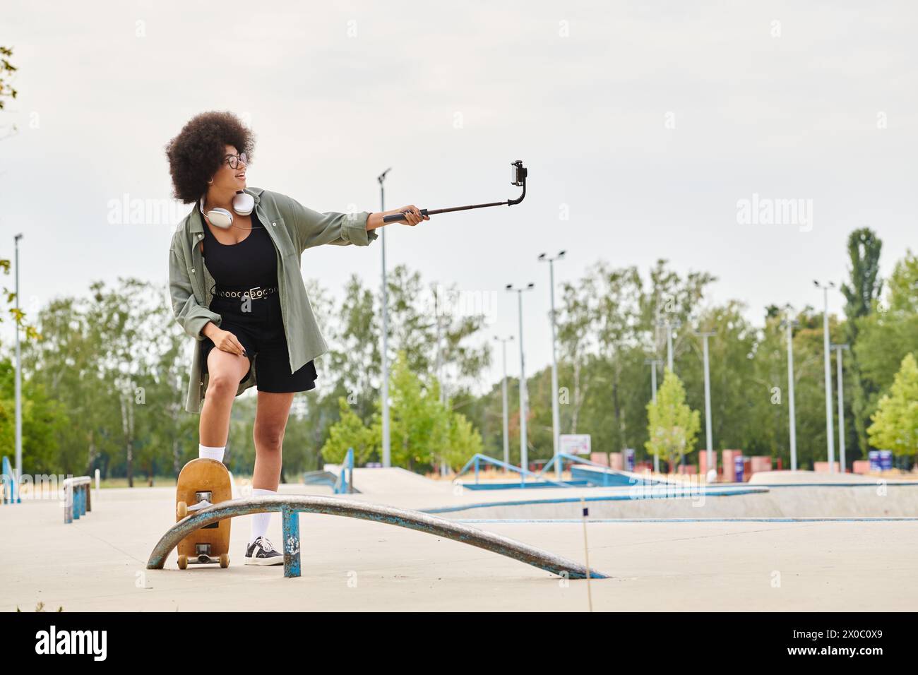 A young African American woman with curly hair skillfully balances on a skateboard at a vibrant skate park. Stock Photo