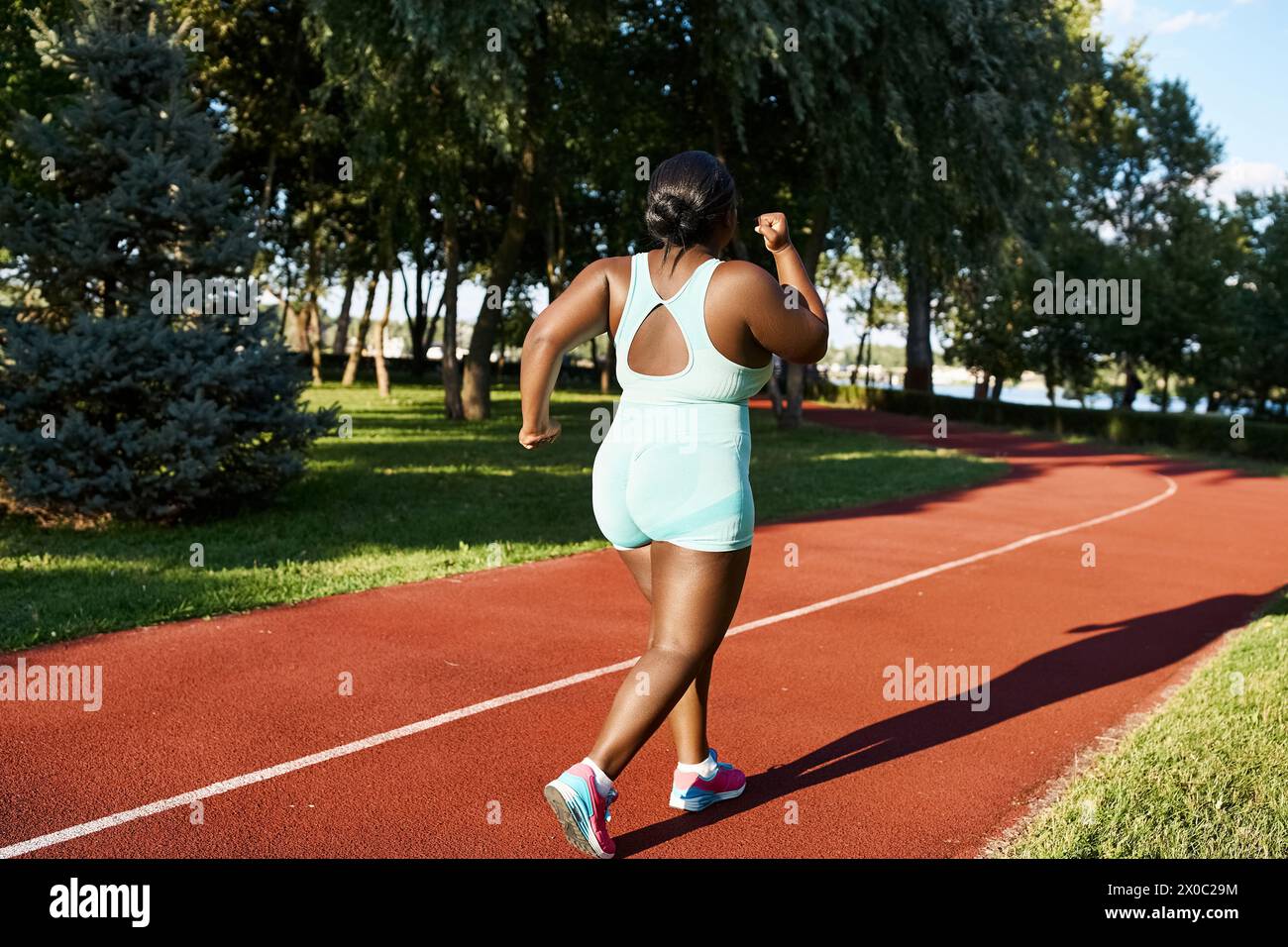 An African American woman in sportswear runs along a red track, showcasing body positivity and athleticism. Stock Photo