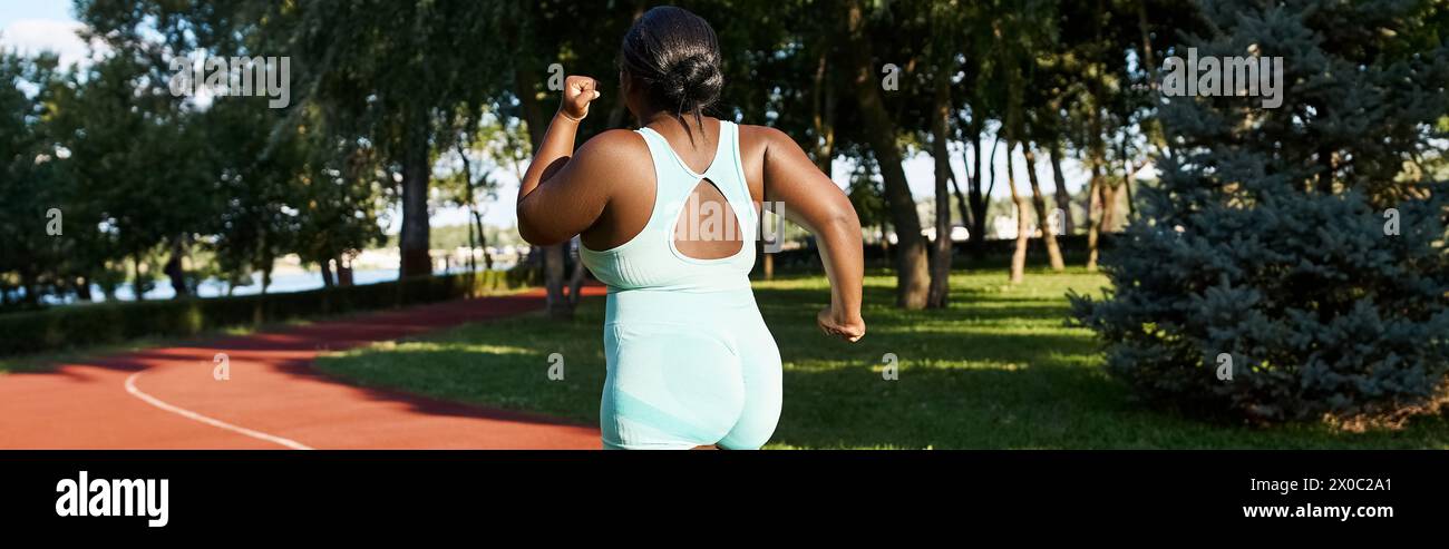 A curvy African American woman in sportswear runs along a red track on a sunny day Stock Photo