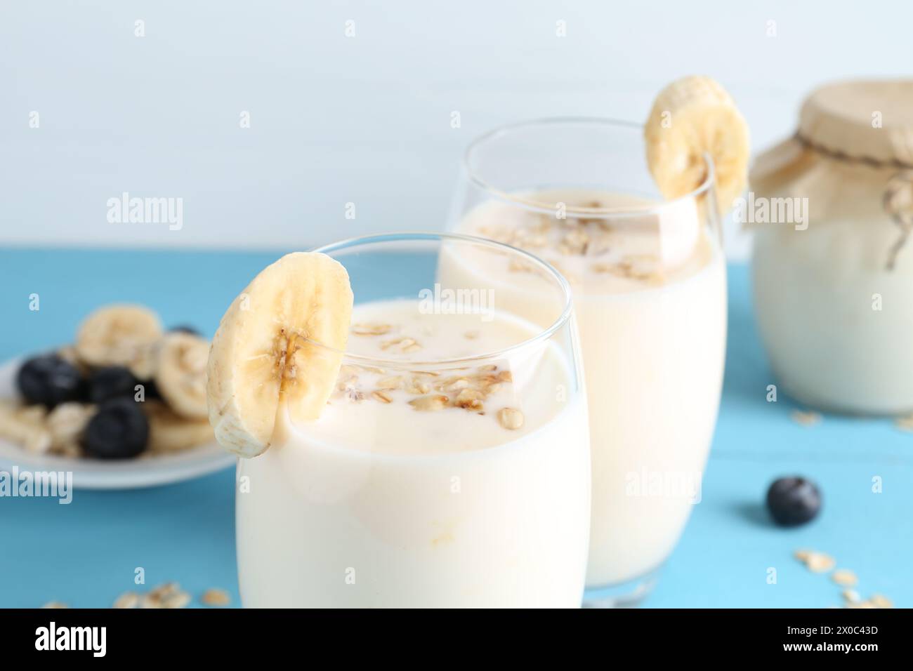 Tasty yogurt in glasses, oats, banana and blueberries on light blue table, closeup Stock Photo