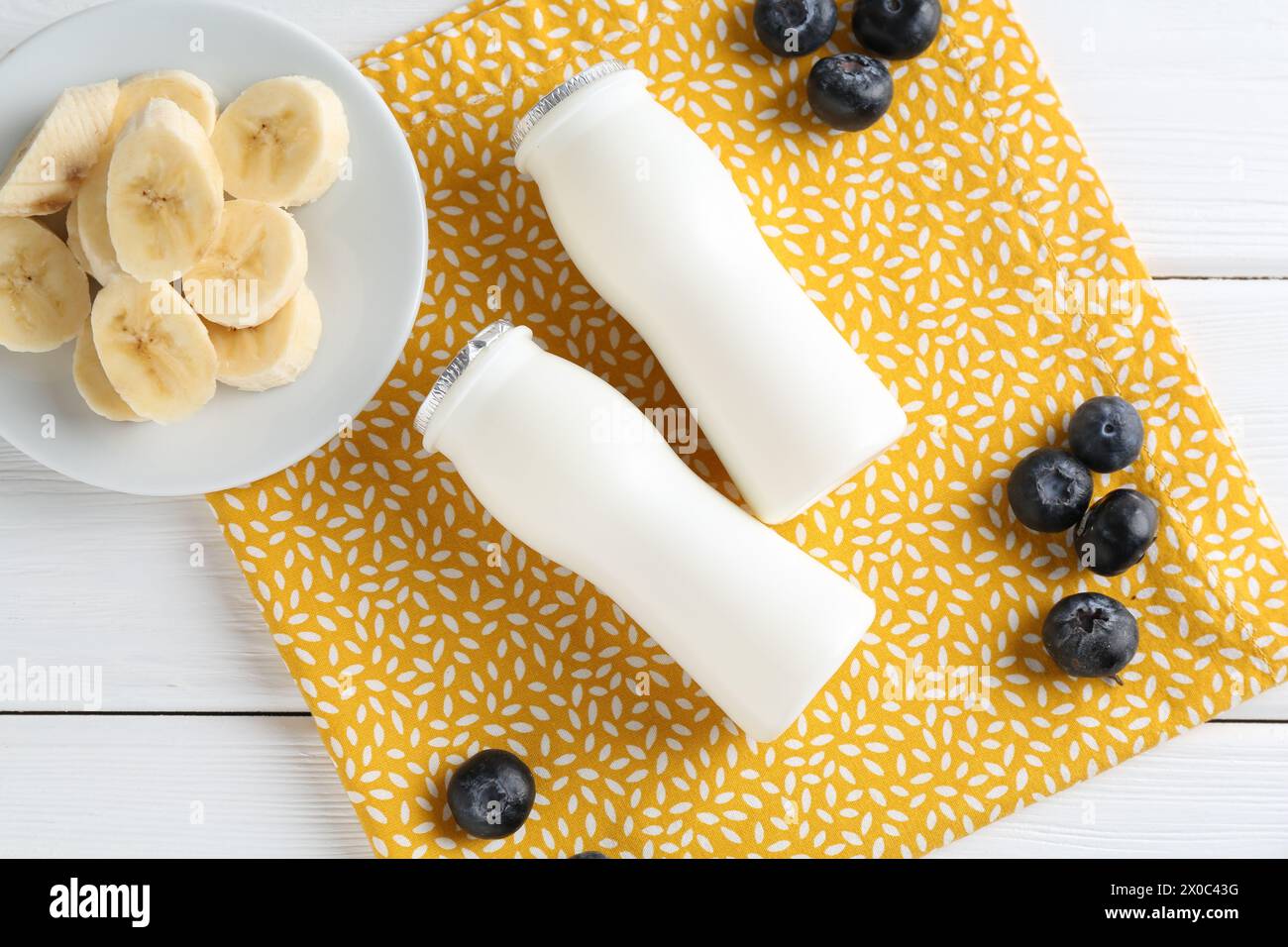 Tasty yogurt in bottles, banana and blueberries on white wooden table, top view Stock Photo