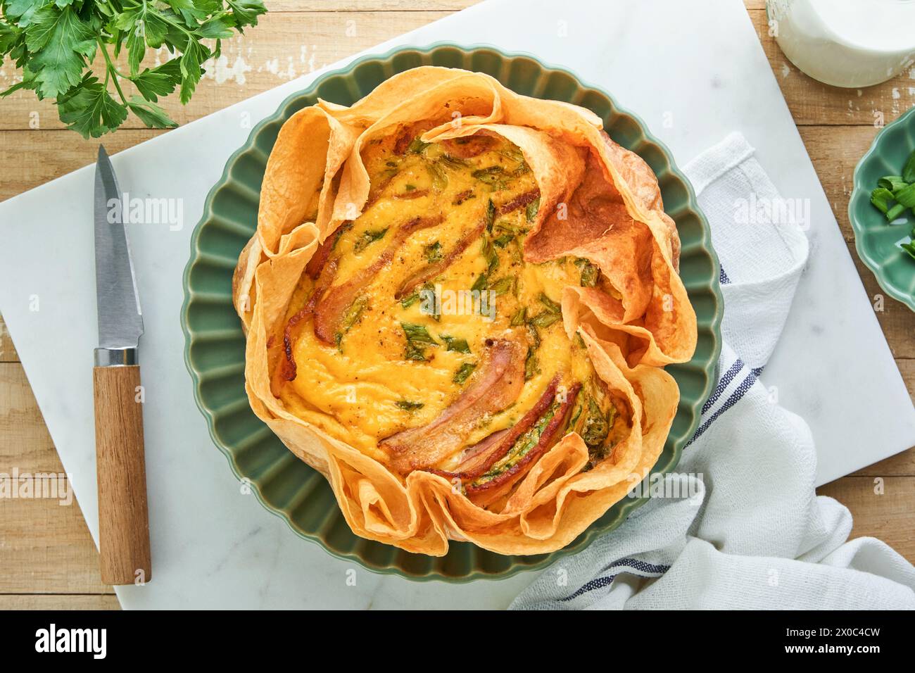 Homemade quiche or tart with slices of bacon and leeks with tortilla instead of dough on wooden cutting board on rustic old wooden background. Quiche Stock Photo