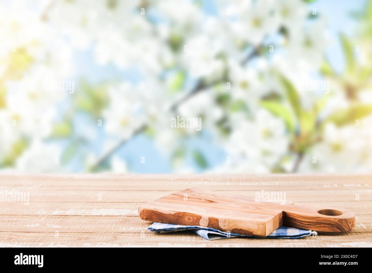 Empty rustic wooden table with blue tablecloth and wooden board over rapeseed blooming summer garden on sunny day background. Harvest mock up for desi Stock Photo