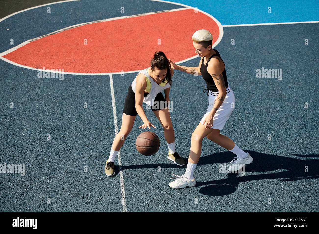 Two athletic young women stand proudly on top of a basketball court, exuding confidence and sportsmanship on a sunny day. Stock Photo