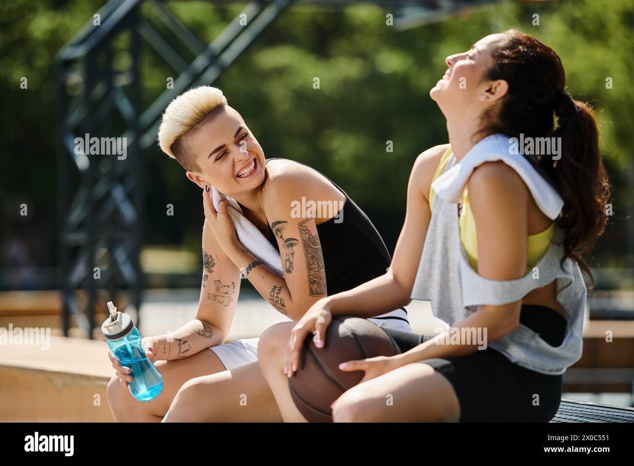 Two young women sitting together after playing basketball outdoors, enjoying a moment of friendship and camaraderie. Stock Photo