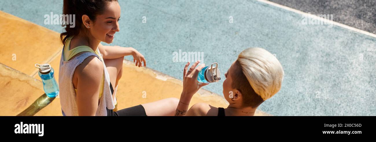 Two young women, sporty and energized, stand side by side on the basketball court in the warm summer sun. Stock Photo