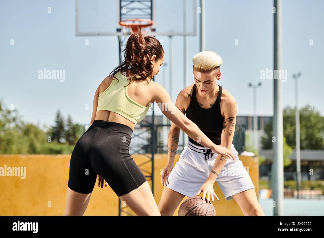 women engage in a friendly game of basketball on an outdoor court, showcasing their athletic skills and competitive spirit. Stock Photo