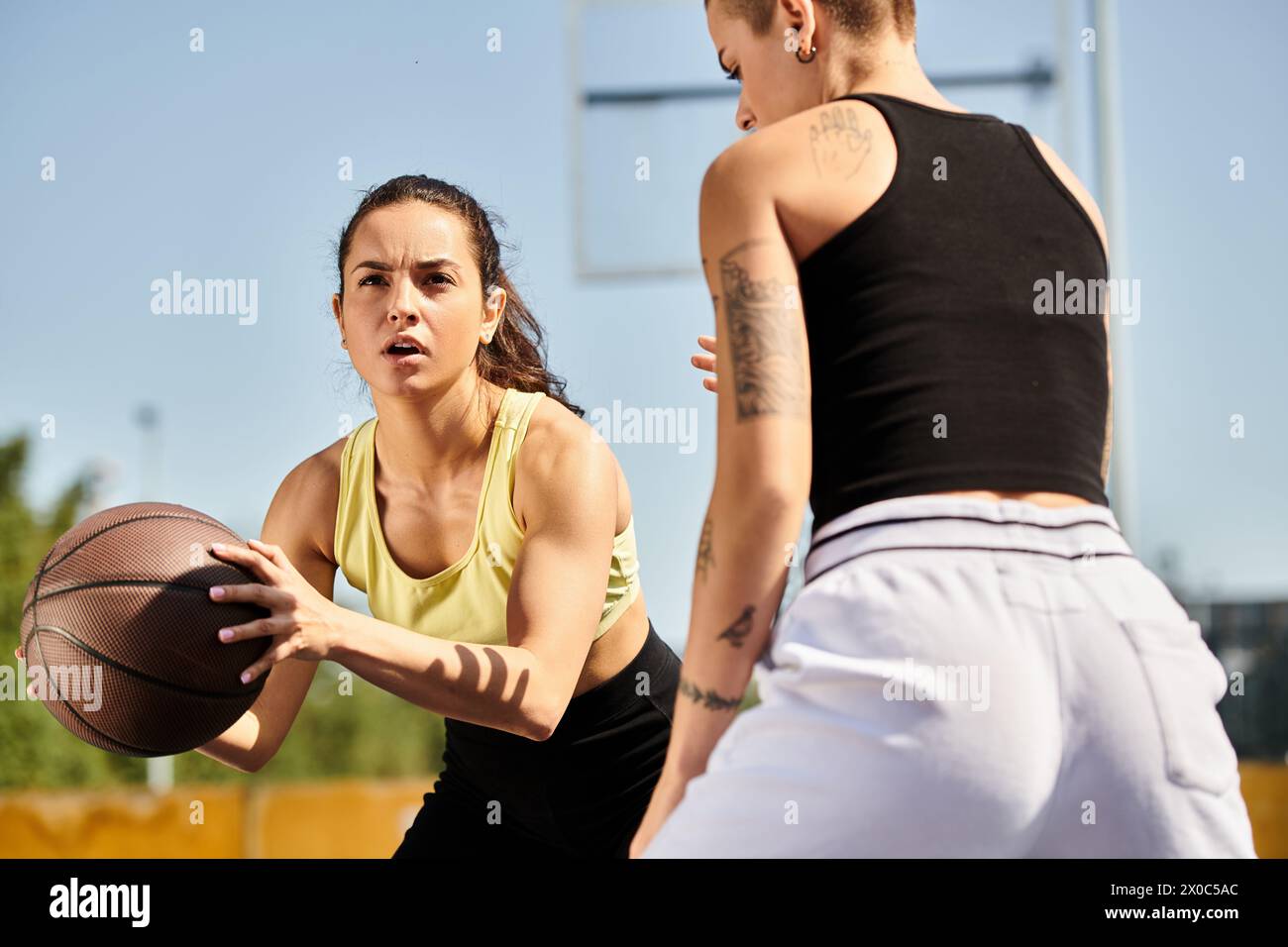 Two athletic young women standing outdoors, one holding a basketball, embodying friendship and sportsmanship on a sunny day. Stock Photo