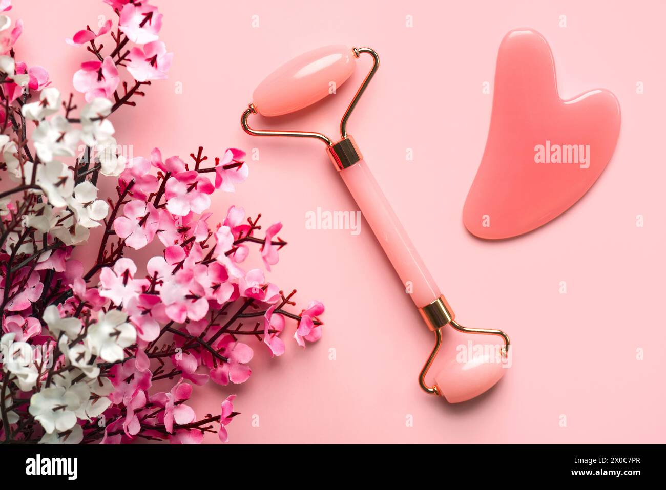 Closeup of pink jade roller, jade gua sha massager stone and almond blossoms against a pink background. Skin care products concept Stock Photo