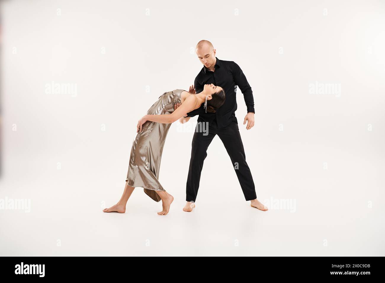 A young man in black and a young woman in a silver dress showcase grace and acrobatic elements in a dance pose. Stock Photo