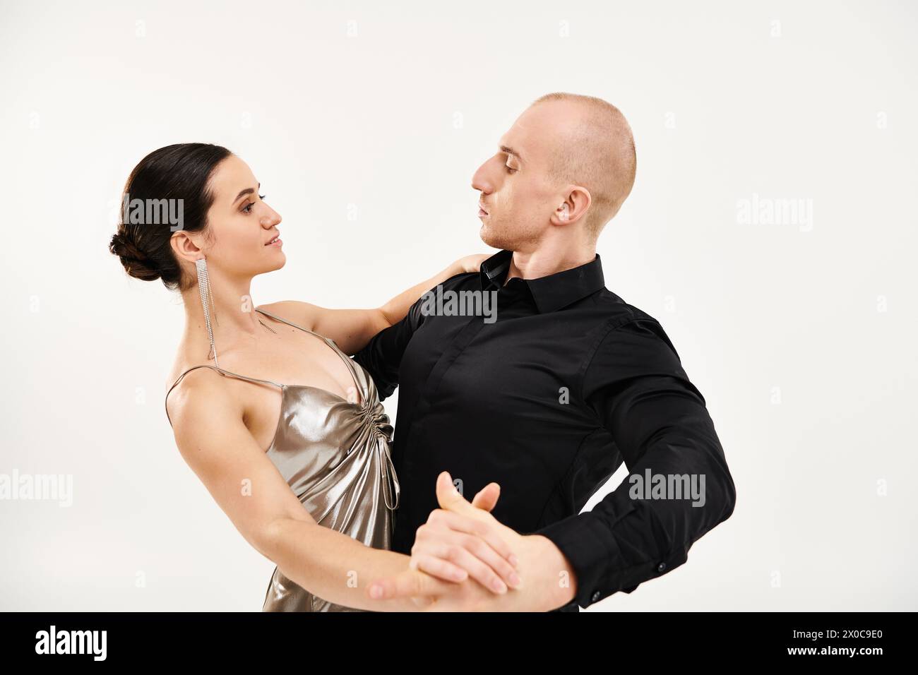 A young man in black and a young woman in a shiny dress dance together in a studio setting with a white background. Stock Photo