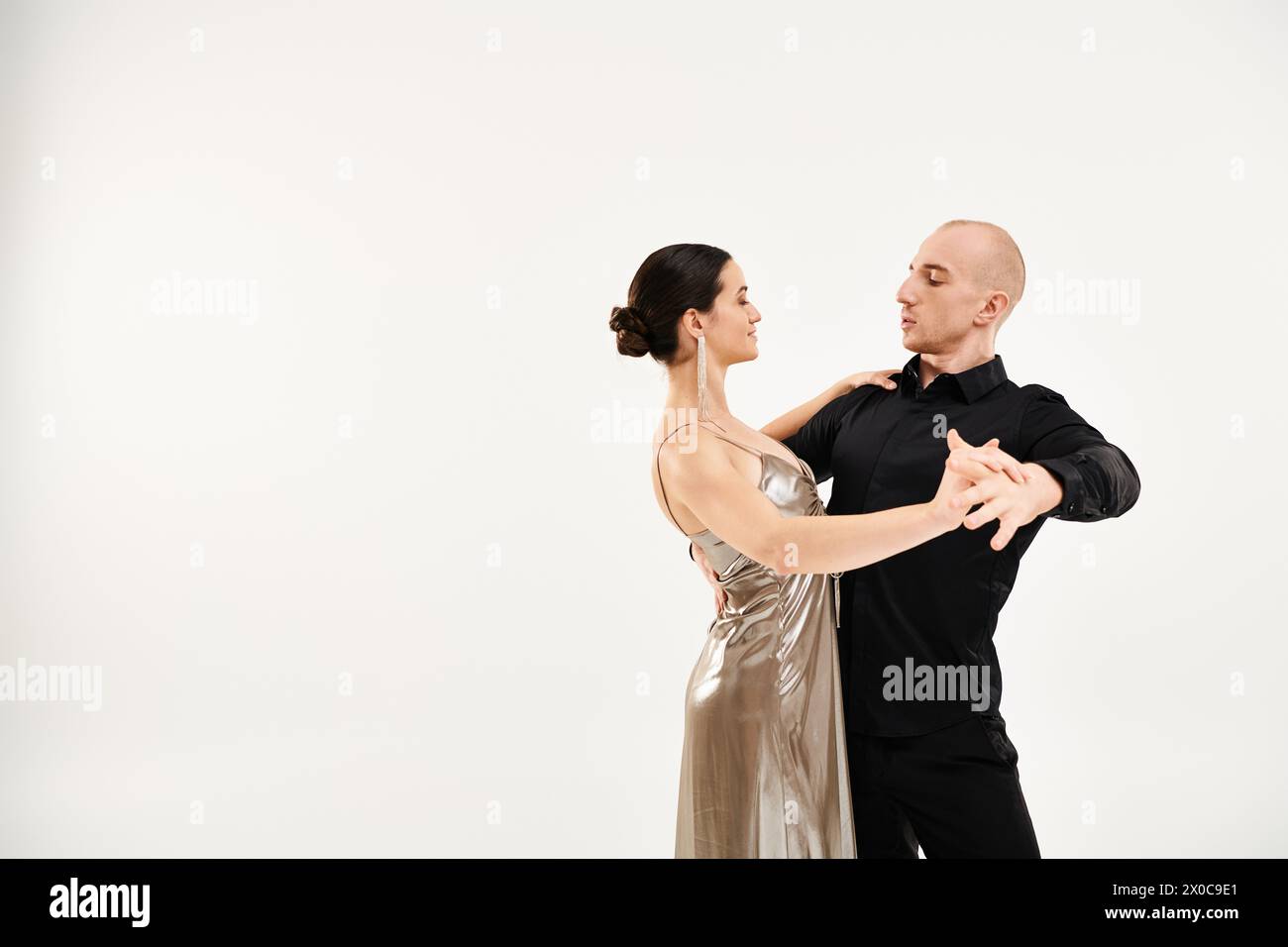 A young man in black attire and a young woman in a shiny dress dance fluidly. Stock Photo