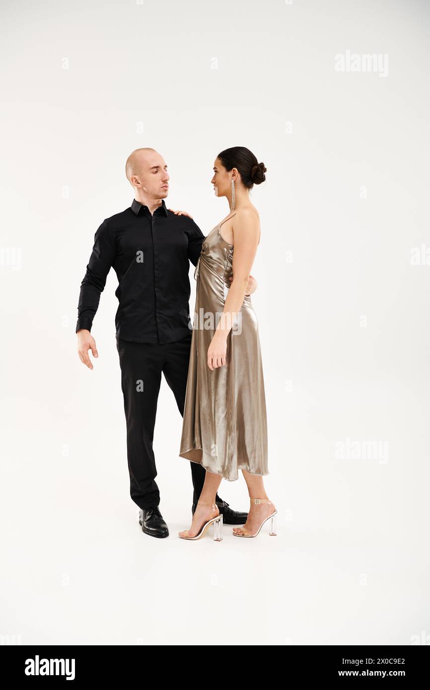 A young man in black and a young woman in a shiny dress perform dance, framed against a white studio backdrop. Stock Photo