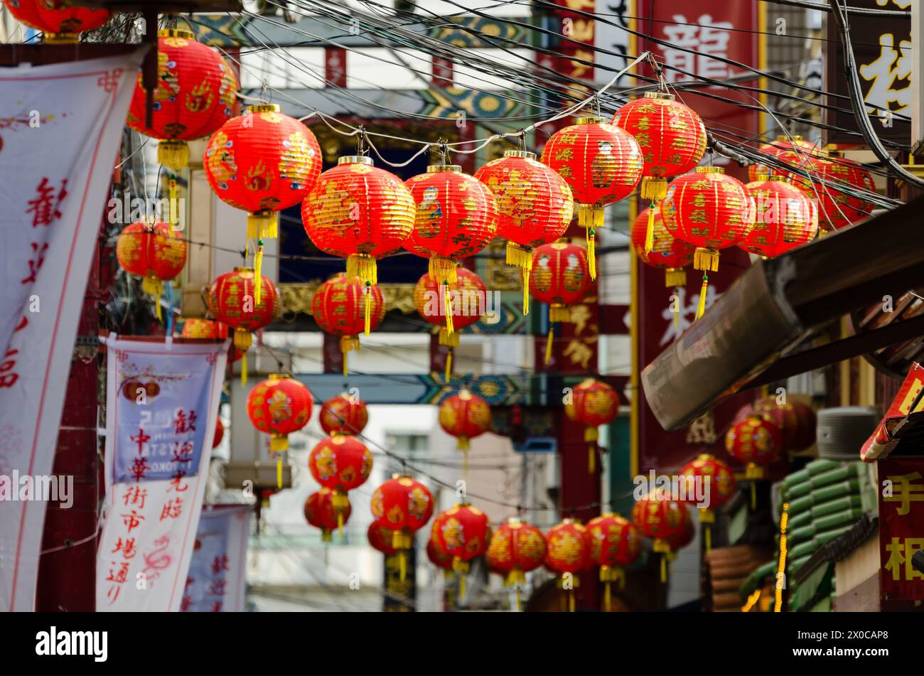 A street with many red lanterns hanging from the wires. The lanterns are red and have Chinese characters on them Stock Photo