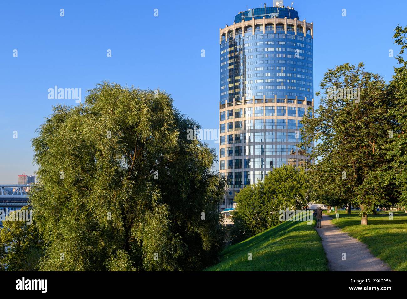 Moscow, Russia - 31 Aug 2017: A modern architectural marvel stands tall, juxtaposed against the serene beauty of lush greenery and a tranquil walking Stock Photo