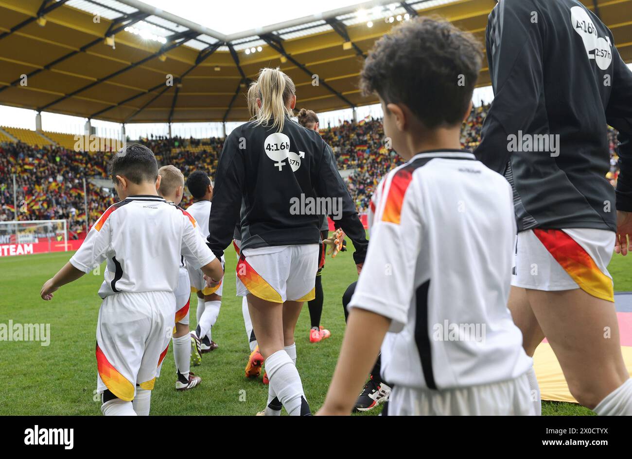 firo : 09.04.2024 Football, Football, 2023/2024 WOMEN'S INTERNATIONAL MATCH EM Euro Qualification EM Qualification Germany - Iceland Entry of the German team with message for women Justice on the tracksuit Sign for equal rights Instead of the logo of the household appliance manufacturer, the numbers '4:16' and '2:57' will be seen on the backs of the national players. With these numbers, the women want to point out an imbalance in the performance of work for the household and family. While women spend an average of 4:16 hours a day on care work, i.e. looking after children, this time is only 2: Stock Photo
