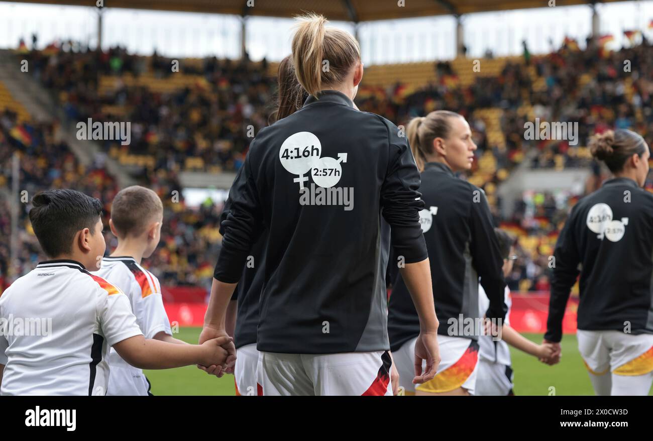 firo : 09.04.2024 Football, Football, 2023/2024 WOMEN'S INTERNATIONAL MATCH EM Euro Qualification EM Qualification Germany - Iceland Entry of the German team with message for women Justice on the tracksuit Sign for equal rights Instead of the logo of the household appliance manufacturer, the numbers '4:16' and '2:57' will be seen on the backs of the national players. With these numbers, the women want to point out an imbalance in the performance of work for the household and family. While women spend an average of 4:16 hours a day on care work, i.e. looking after children, this time is only 2: Stock Photo