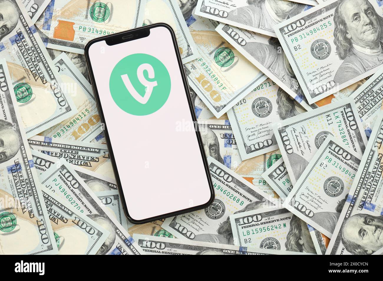 KYIV, UKRAINE - APRIL 1, 2024 Vine icon on smartphone screen and many usd money bills. iPhone display with app logo and lot of hundred dollars banknotes close up Stock Photo