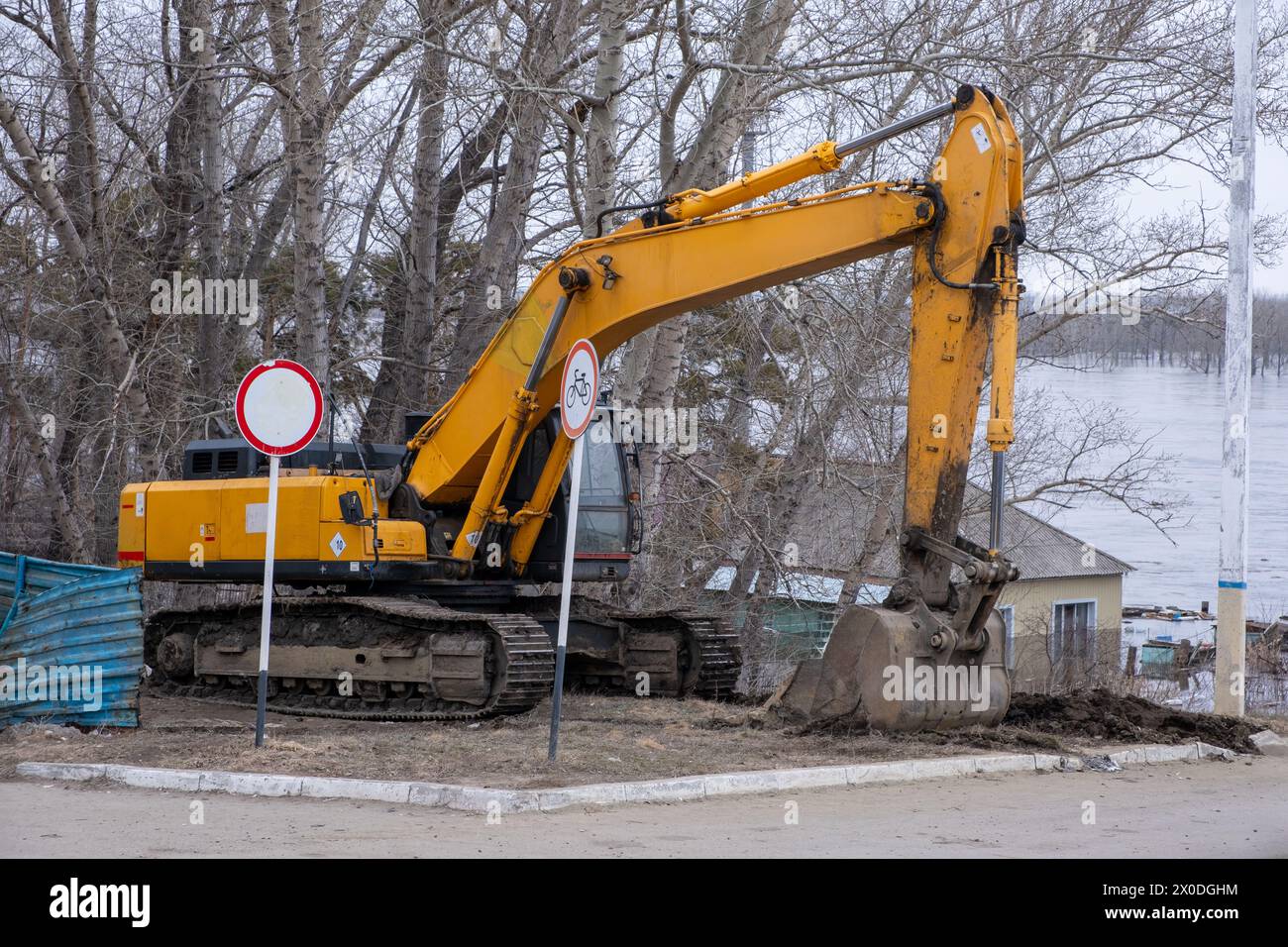 Excavator stands against background flooded house during spring flood. Heavy machinery Stock Photo