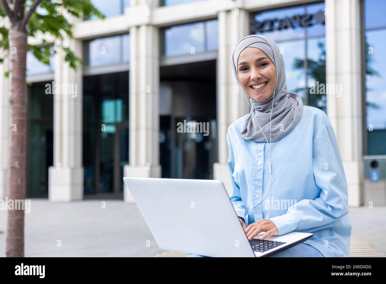 Smiling professional woman wearing a hijab works on her laptop, seated ...