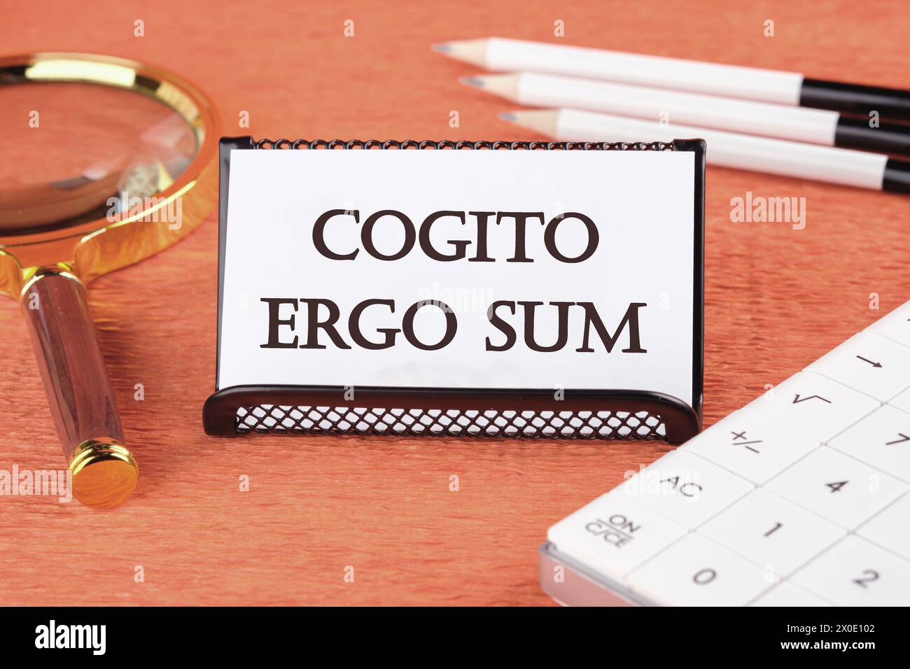 The words Cogito Ergo Sum or I think Therefore I Am there is a magnifying glass, a calculator, and pencils on a white business card next to it Stock Photo
