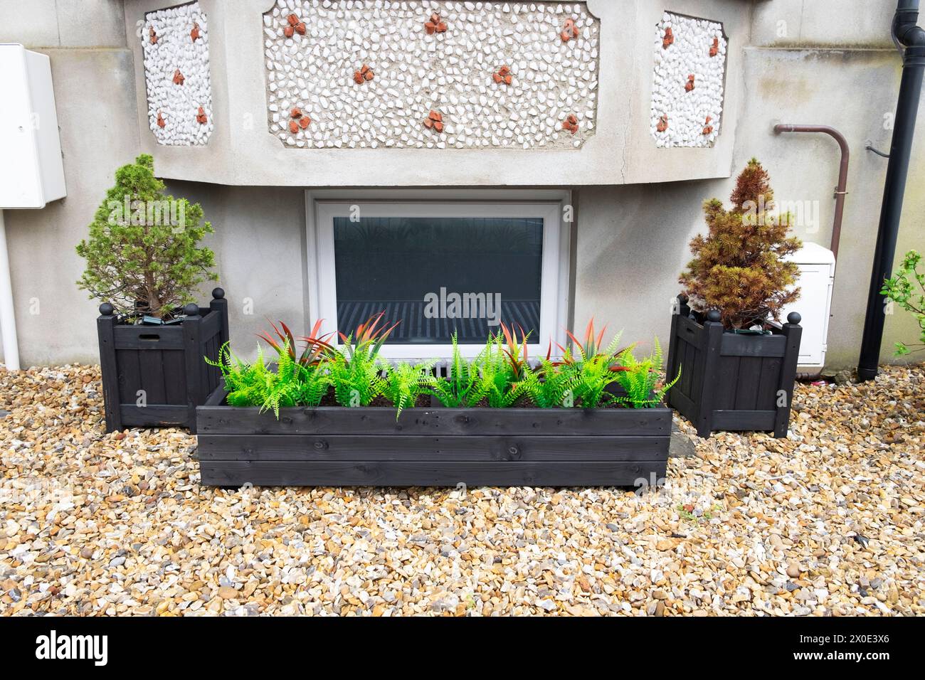 Kitsch plastic fake artificial foliage plants ferns in fake wooden container outside in front garden of home house pebbles not lawn UK  KATHY DEWITT Stock Photo