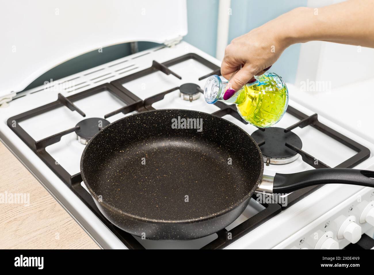 housewife pours frying oil into a frying pan. oil at the bottom of the pan. frying pan in the kitchen. Stock Photo